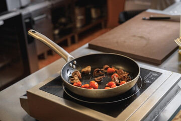 Tomatoes and mushrooms is cooking in frying pan in restaurant kitchen