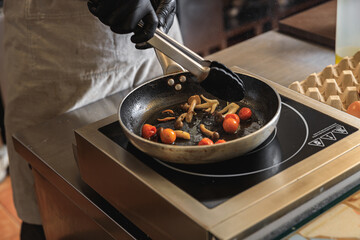 Close up of chef cooking on frying pan tomatoes and mushrooms in restaurant kitchen
