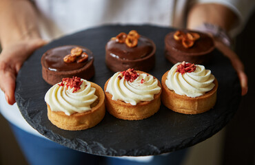 Chef holding a black slate dish with decorated shortbread cupcakes. Delicious pastry products for lunch