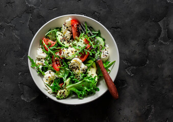 Simple salad with fresh vegetables, avocado and mozzarella on a dark background, top view