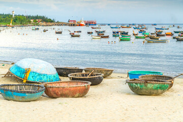 Basket boats spread out on a beach with many fishing boats behind in a calm bay at Da Nang in Vietnam