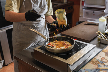The professional chef in uniform adds spices into pan with dish in restaurant kitchen