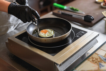 Professional kitchen worker cooking egg on a frying pan to make delicious breakfast
