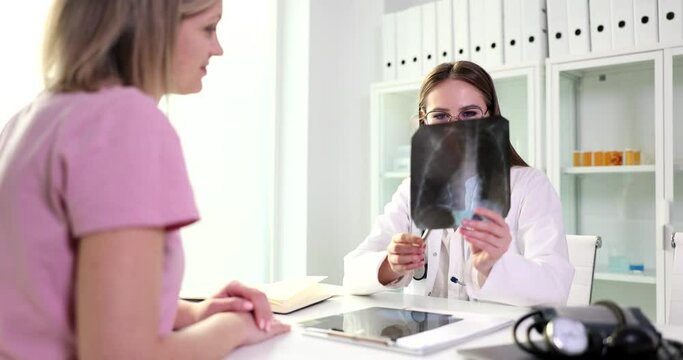 Professional doctor shows female patient x-ray image of lungs in office. Specialist prescribes treatment for woman patient at appointment slow motion