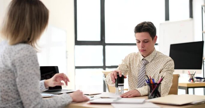 Clerk puts stamp on customer document in company office slow motion. Manager approves official contract papers for client at workplace