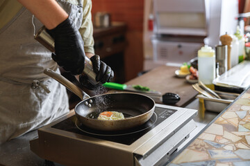 Professional kitchen worker cooking egg on a frying pan to make delicious breakfast