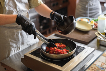 Close up of chef in uniform is cooking dish on frying pan for client order on restaurant kitchen