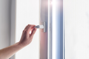 A man's hand holds a plastic window handle.Manual opening white plastic pvc window at home.A man opens a window, closes a plastic frame in his apartment. Roll-up blinds to protect against sunlight.