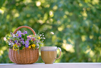 flowers bouquet in wicker basket and cup close up on table in garden, abstract natural green background. spring, summer season. rustic still life with meadow flowers. template for design. copy space - Powered by Adobe
