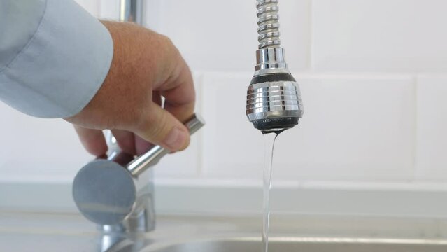 Man Shuts the Water Tap, Stopping Flowing Water in the Kitchen Sink.