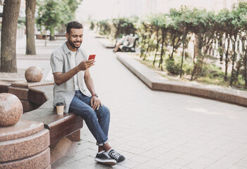 Young student man using smartphone in a city. Smiling joyful guy summer portrait. Handsome man looking at mobile phone