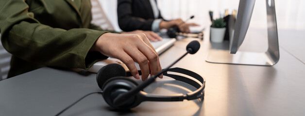 Panorama focus hand holding headset on call center workspace desk with blur background of operator team or telesales representative engaging in providing client with customer support service. Prodigy
