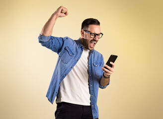 Excited businessman dressed in denim shirt screaming and raising hand while reading good news over...