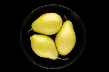 Three organic pears in a black ceramic plate isolated on a black background, top view, macro.