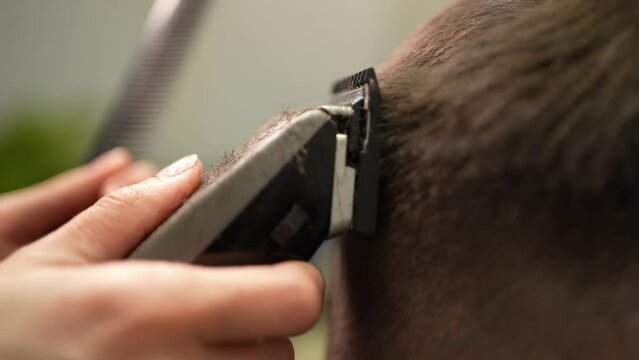 A hairdresser makes a man's hairstyle with a clipper