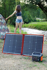 Woman at camping out in nature uses solar panel and power generator for independent electricity	
