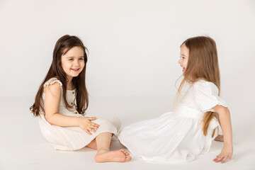 Cute kids, portrait of happy little girls in white summer dresses on white background. Children fashion, style concept. A happy childhood, children's world, the concept of stylish children's clothing