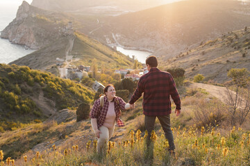 Tourists: A couple travels through the spring mountains. A man in a plaid shirt gives his hand to help a plump woman up the mountain. Walks in the open air. Travel and active life concept. Travel life