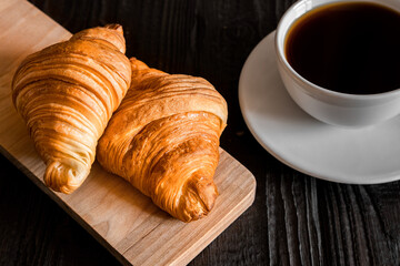 Coffee cup with croissant on a rustic dark wooden table. Food series. Two tasty fresh croissants, jam, orange juice. Continental breakfast served with freshly baked pastry. Close up view, Good morning