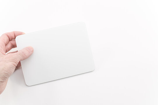 immagine editoriale illustrativa di mano che sorregge, mostra periferica Apple Magic Trackpad su superficie di lavoro bianca