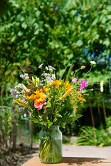 Floral minimalist greeting card. Bright meadow flowers in a glass jar vase on a table outside. Happy mother's day, women's day or birthday. Village theme.	
