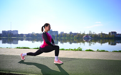A young woman exercising at a tranquil lake during a beautiful morning. She's wearing workout...