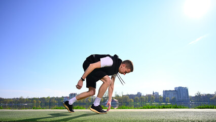 A young man stands by the lake in the morning, dressed in sportswear, ready for a run. His trainers are lightweight and look well-worn, indicating his dedication to his fitness routine.