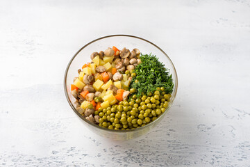 Glass bowl with vegetarian olivier salad of potatoes, carrots, onions, pickles, mushrooms, green peas and dill on a light blue background, top view. cooking stage