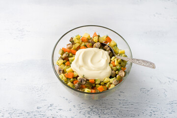 Glass bowl with vegetarian Olivier salad of potatoes, carrots, onions, pickles, mushrooms, green peas, dill with mayonnaise on a light blue background, top view. cooking stage - 597417289