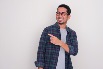 Adult Asian man looking and pointing behind with happy expression