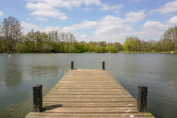 Naklejka premium view over wooden jetty over small lake with surrounding trees. peaceful scene in outdoor park space 