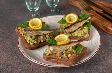 Homemade Guacamole sandwiches with sprats and lemon on round plate on brown background