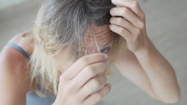 A woman examines her cropped hair with the first signs of gray hair and spoiled after highlighting