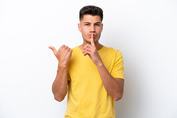 Young caucasian man isolated on white background pointing to the side and doing silence gesture