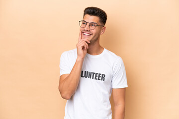 Young volunteer caucasian man isolated on beige background thinking an idea while looking up