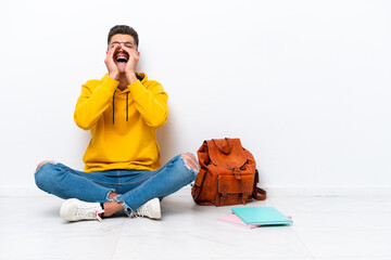 Young student caucasian man sitting one the floor isolated on white background shouting and announcing something