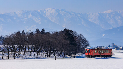 雪の荒島岳を背景に越前富田を走る越美北線のオレンジ色の単行気動車