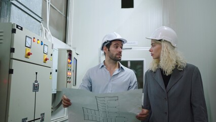 Two industry engineers in construction helmets looking project blueprints while walking in warehouse