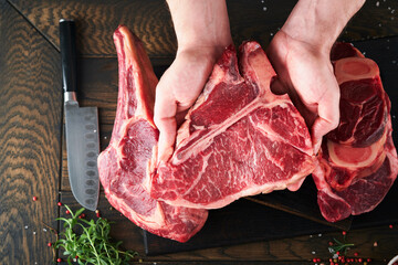 Steak beef meat. Chef cutting steak beef. Mans hands hold raw steak Tomahawk on rustic wooden...