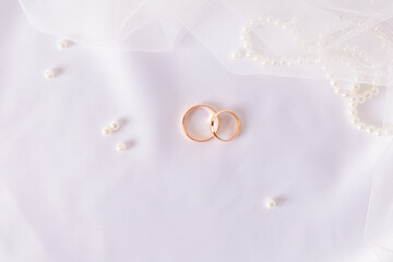 Two gold wedding rings on a chic white satin background with a pearl necklace and veil . wedding background. layout for design.