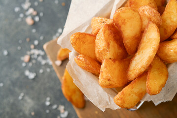 French fries in metal wire basket with salt and ketchup on old wooden dark background clous up. Fried potatoes. Fast food and unhealthy food concept.