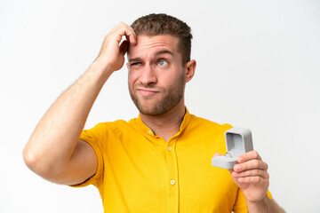 Young man holding a engagement ring isolated on white background having doubts and with confuse face expression