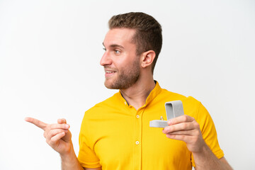 Young man holding a engagement ring isolated on white background pointing to the side to present a product