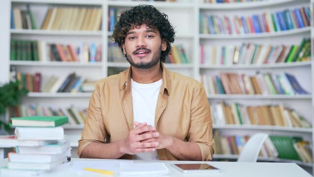 Young happy teacher student having online video call training in campus library space. A college or university tutor starts a webinar, a lesson, has a classroom meeting while looking into the camera