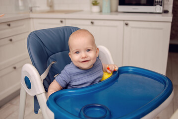 A sweet baby dressed in blue clothing smiles, radiating innocence and happiness in a domestic room as they look into the camera.