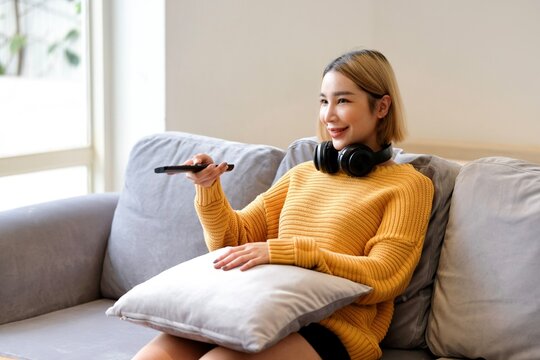 Asian young beautiful woman watching fun movie on television at home. Attractive casual girl feel happy and relax, sit on sofa having fun watch comedy video on TV in house. Activity lifestyles concept