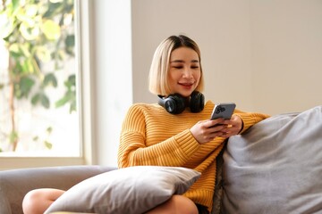 Asian young beautiful woman playing mobile game on smartphone at home. Attractive casual girl feel happy and relax, sit on sofa having fun touching screen on phone to play video enjoy victory in house