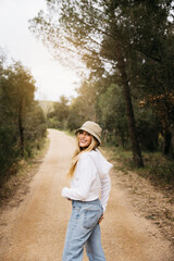 Beautiful blonde woman wearing a hat happily walking on a path in a forest 