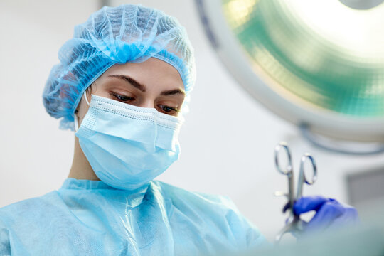 Close-up image of young woman, doctor, surgeon in protective medical mask leading surgery in medical clinic, hospital in surgery room. Concept of medicine, hospital, healthcare, treatment, profession