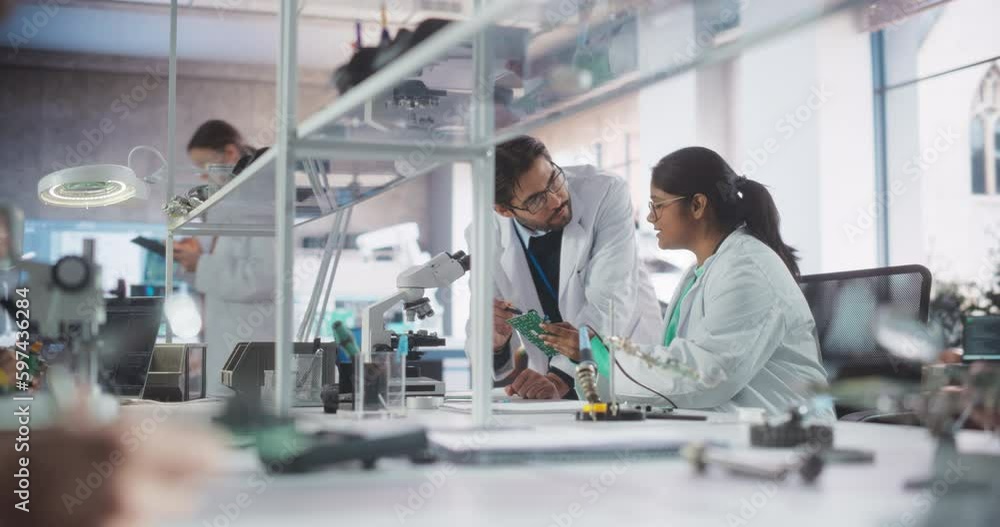 Poster Two Diverse Multiethnic Colleagues Chatting in Laboratory, Working on a Circuit Board for a Computer. Young Indian Scholar Talking with a Scientist About Inserting Different Microchips and Conductors